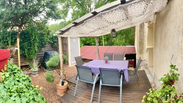 En udendørs terrasse med et bord og stole, omgivet af plantekasser og et træterrasse.