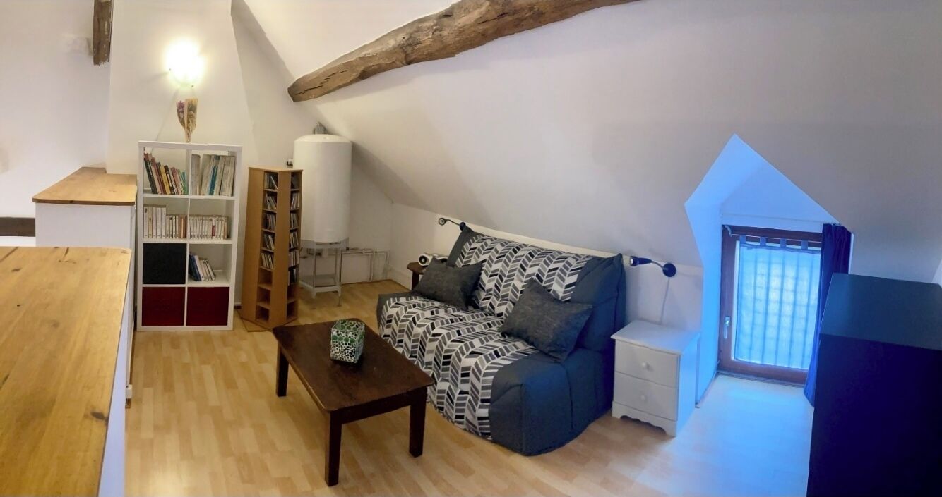 A loft-style room with a wooden floor, a sofa, a coffee table, a bookshelf, a lamp, and a window with blinds.