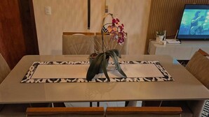 A dining table with a decorative centerpiece, a television in the background, and a potted plant on a side table. - Cozy house in Angra dos Reis (Angra dos Reis)