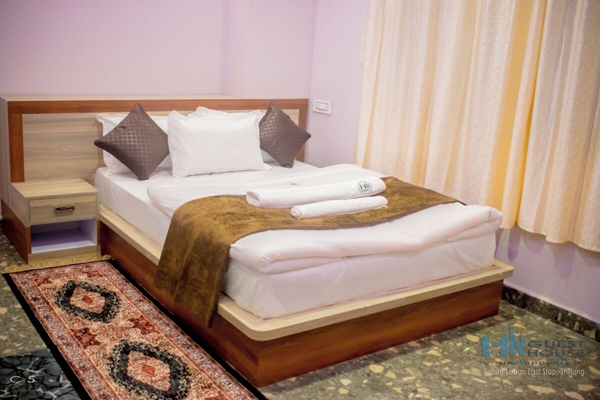 A neatly made bed with pillows, a wooden headboard, a nightstand, and a patterned rug.