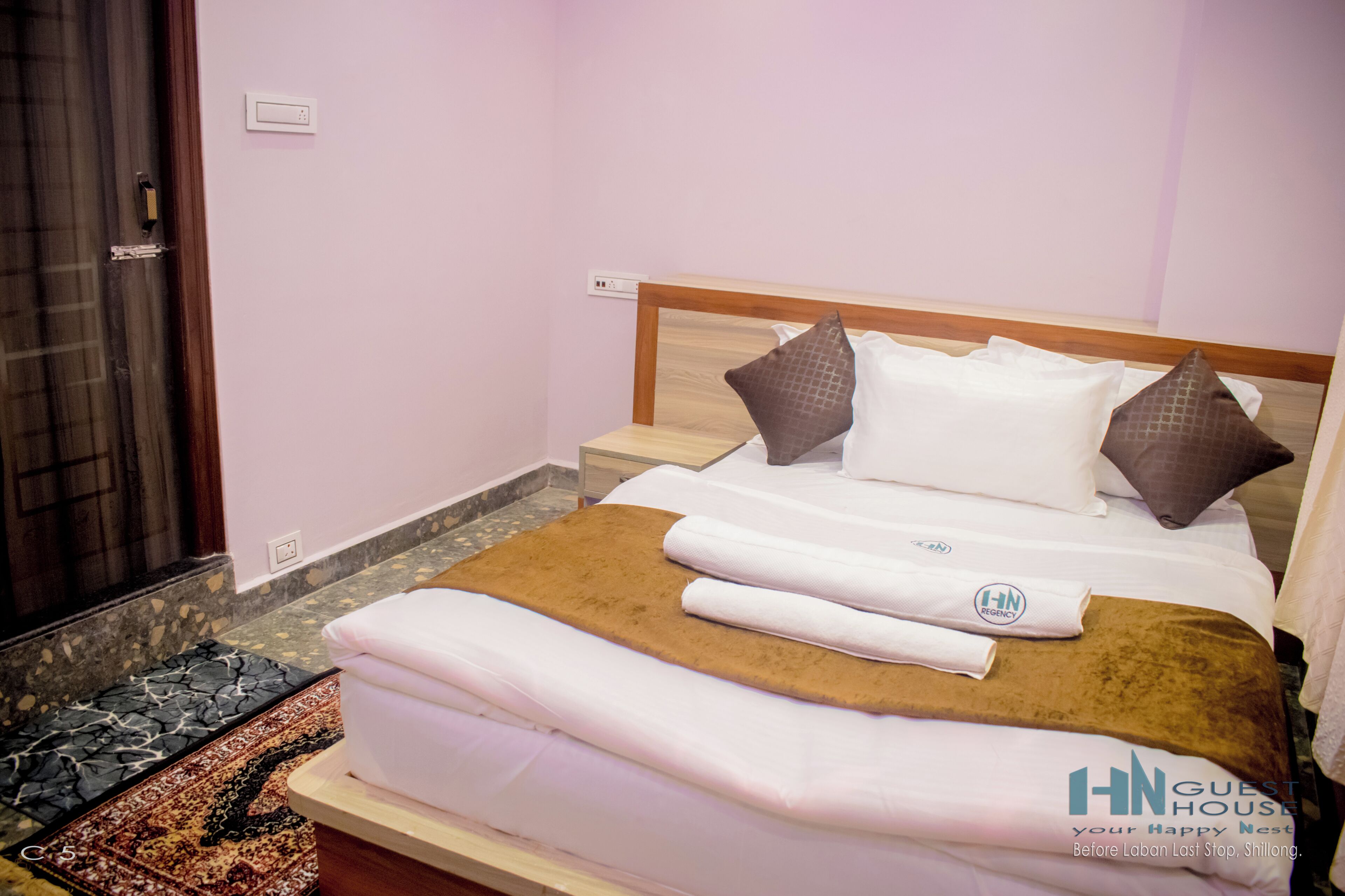 A hotel room with a bed, pillows, a brown rug, and a white towel.