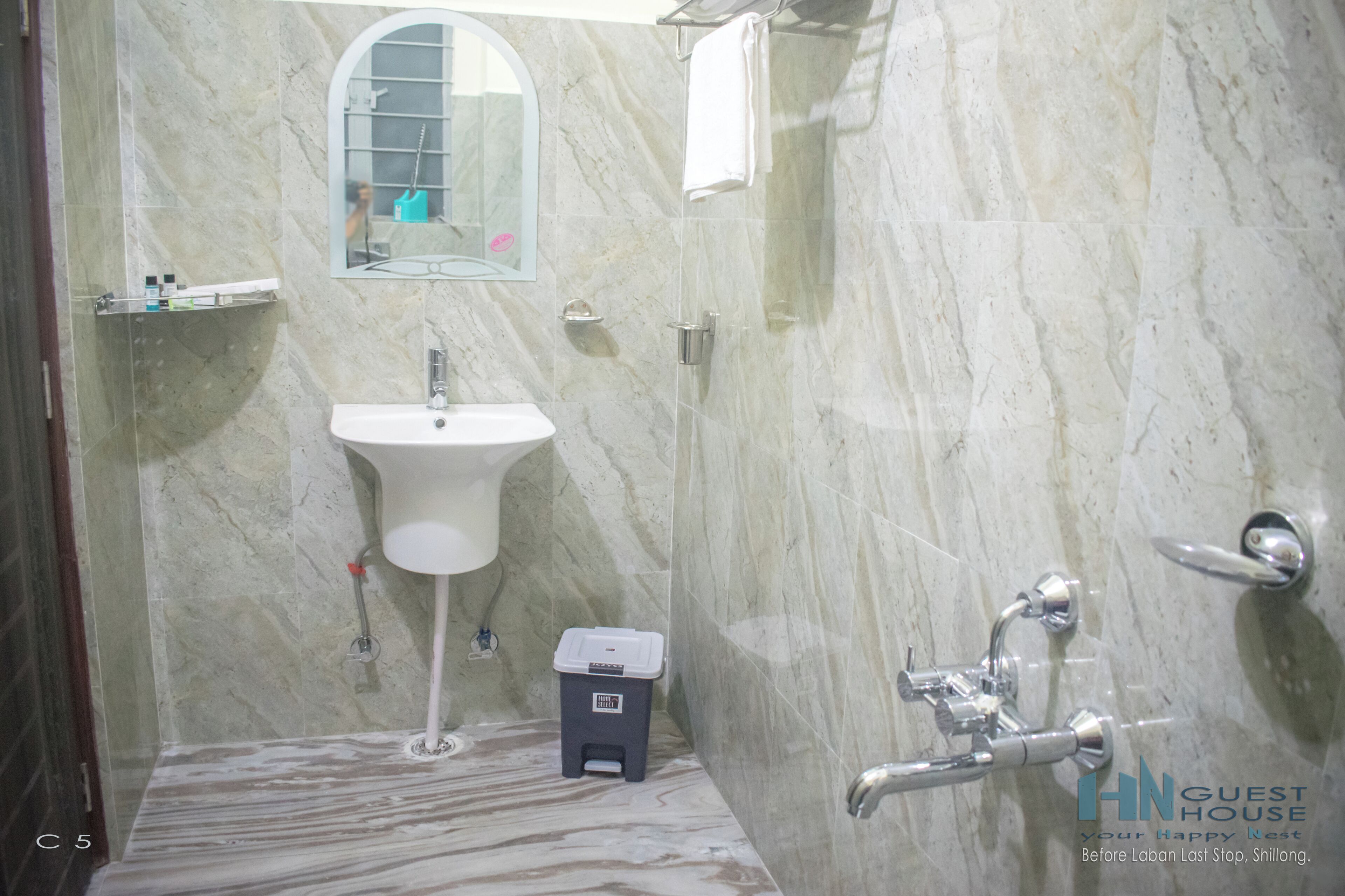 A bathroom with a marble wall, a sink, a mirror, and a shower.