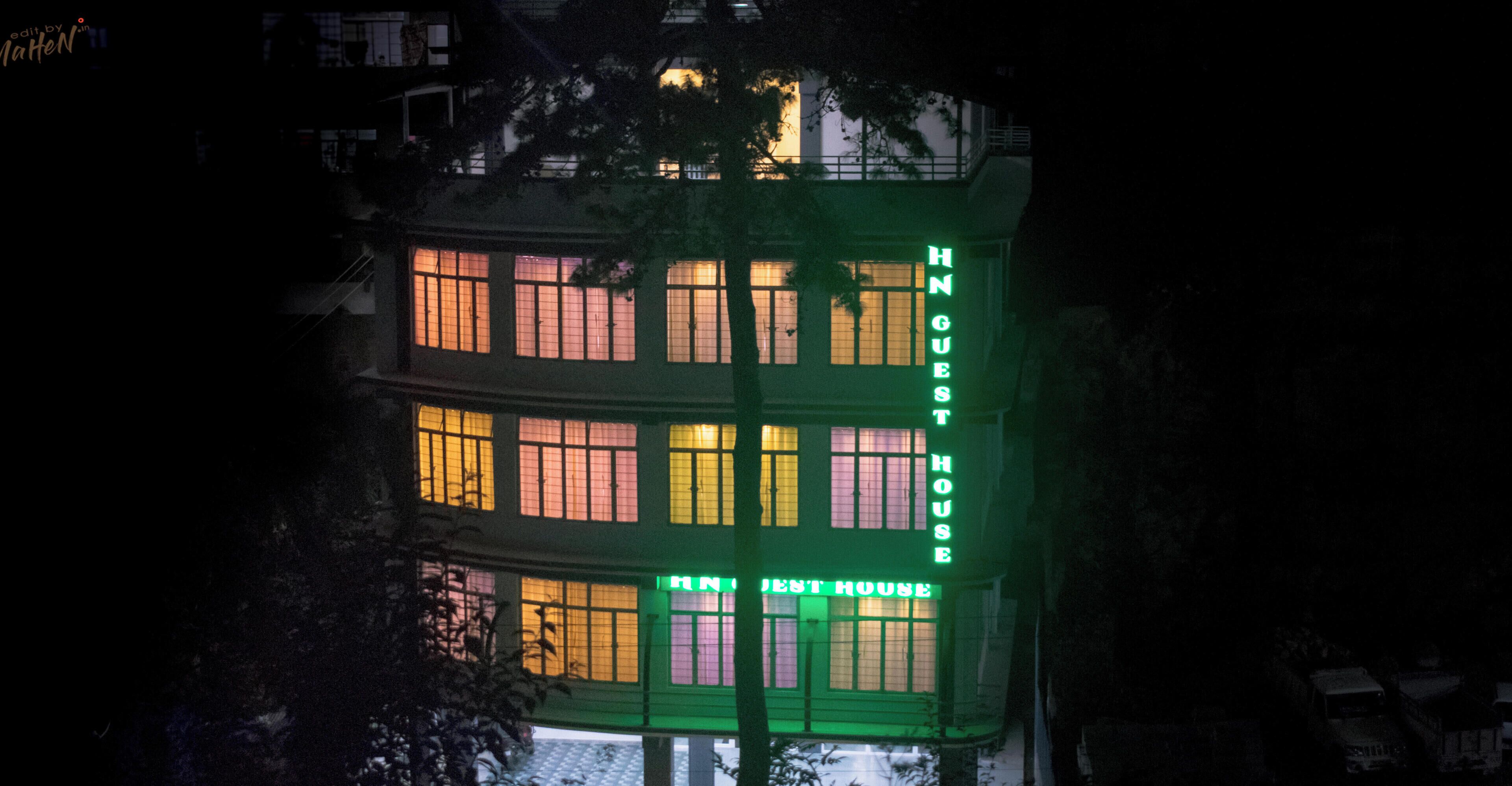 A multi-story building with illuminated signage reading 'HNGUEST HOUSE.'