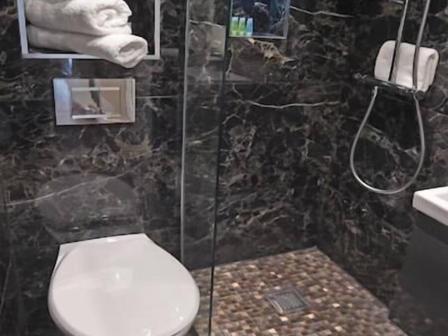 A modern bathroom with a marble wall, a toilet, a glass-enclosed shower, and a towel rack.
