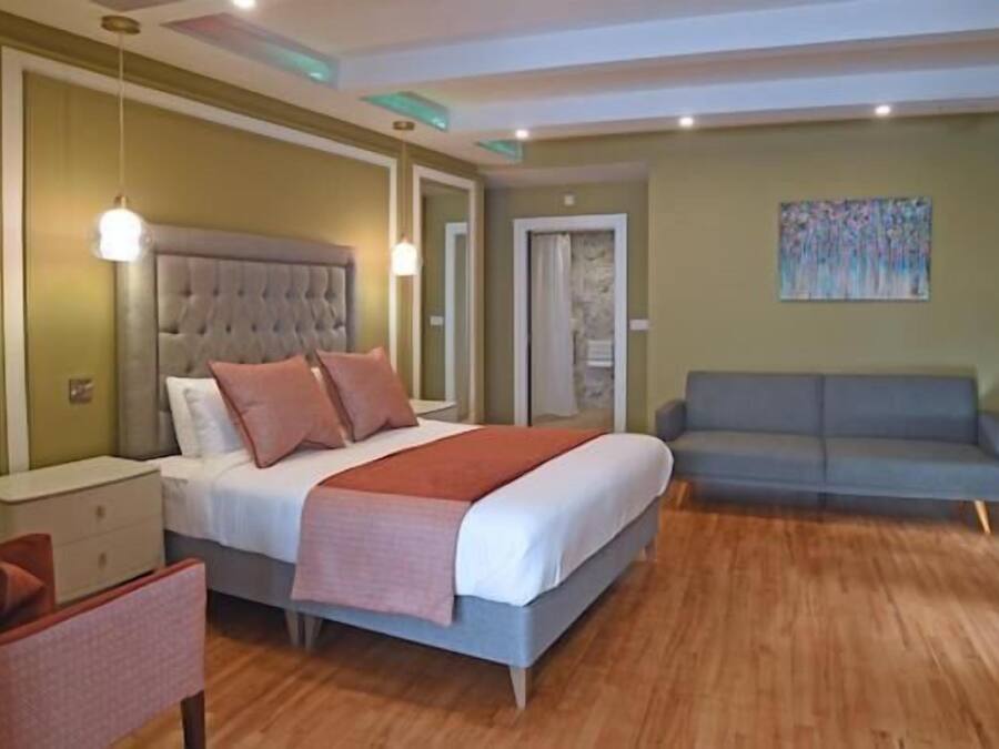 A bedroom with a bed, bedside tables, a chair, a sofa, and a painting on the wall.