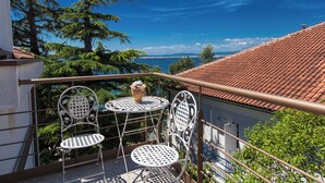 A balcony with two metal chairs and a table, overlooking a coastal view with trees and a tiled roof. - Modern, fully equipped studio in a top location (Crikvenica)