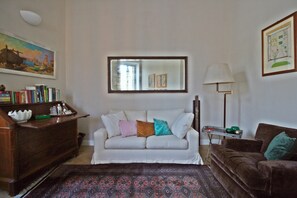 Ein Wohnzimmer mit einem weißen Sofa, einem braunen Sofa, einem Holzschrank, einer Stehlampe und einem gemusterten Teppich.