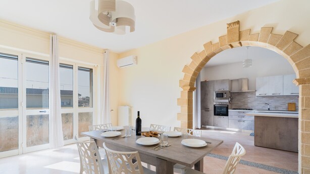 Un coin repas avec une table dressée pour quatre personnes, une bouteille de vin et une vue sur l’extérieur à travers une porte vitrée.