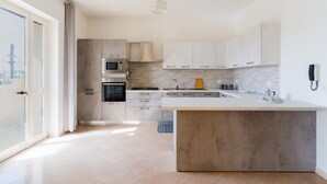 Une cuisine moderne dotée d’un grand îlot central, d’appareils électroménagers intégrés et offrant une vue sur un pont à l’extérieur.