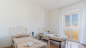 Une chambre avec deux lits, une table de chevet, une lampe et une porte-fenêtre coulissante donnant sur un balcon.