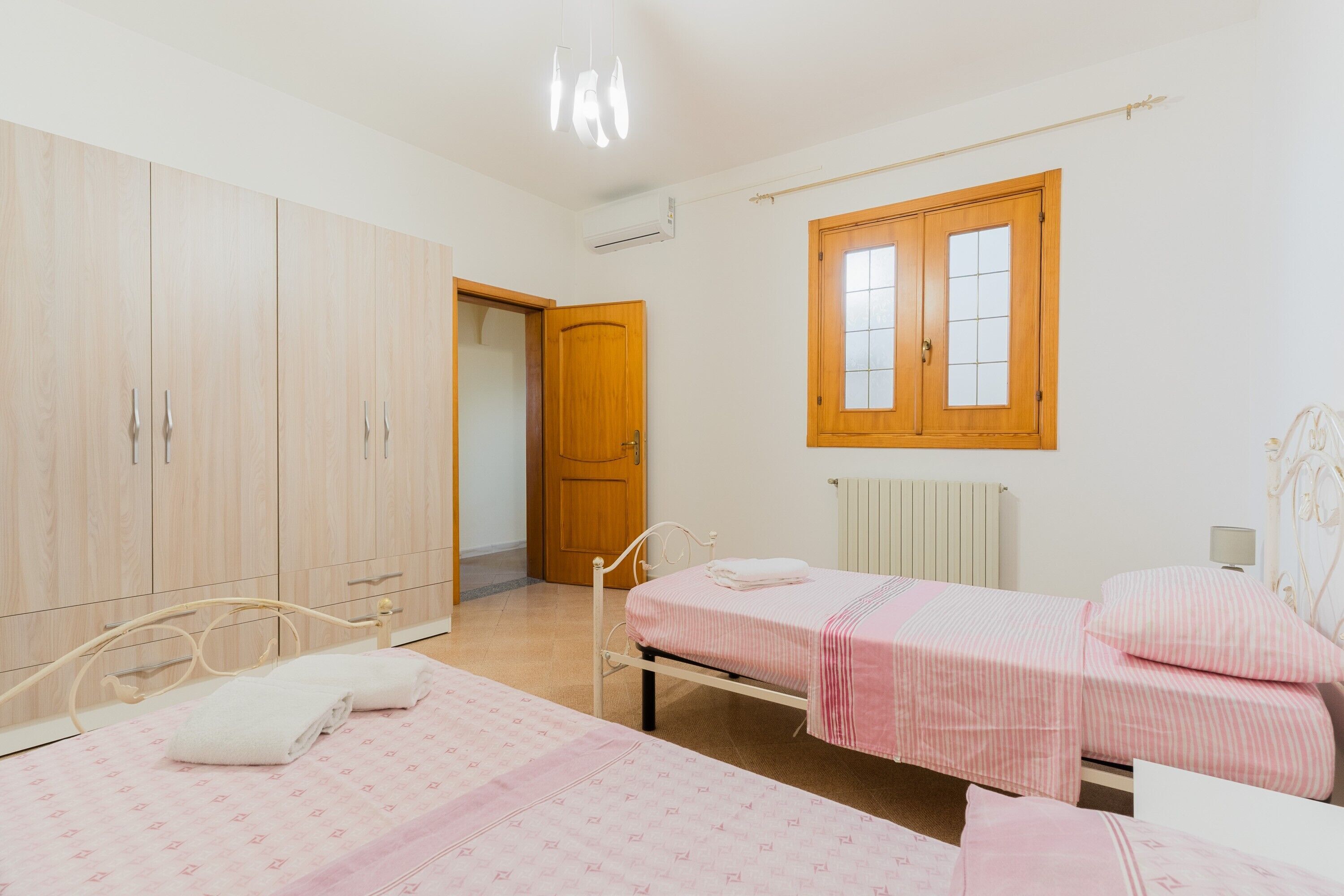 Un dormitorio con dos camas, un armario, una ventana y un aire acondicionado.