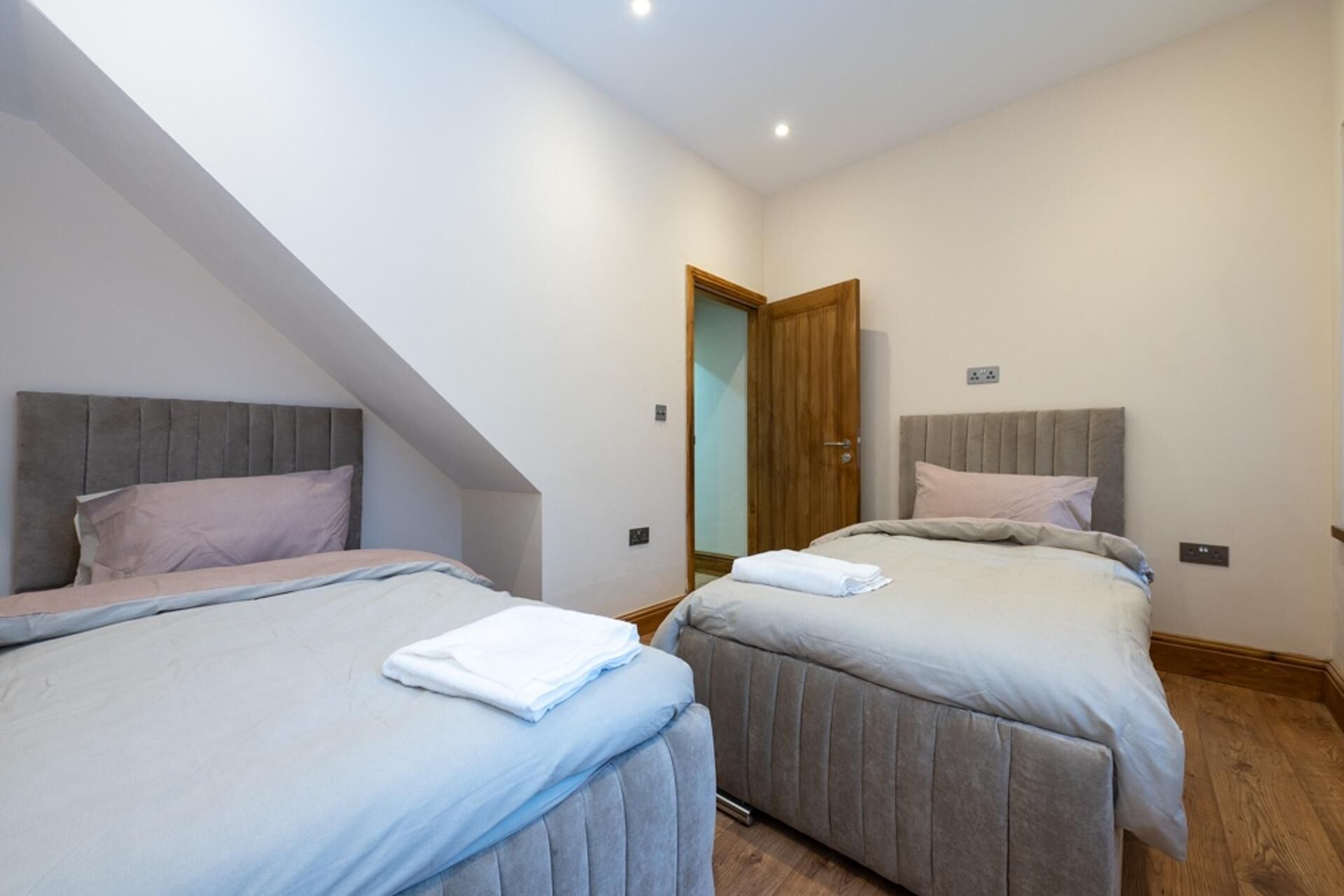 A bedroom with two beds, a wooden door, and a small electrical outlet on the wall.