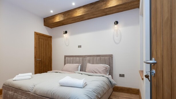 A bedroom with a bed, wooden ceiling beams, two wall-mounted light fixtures, and a wooden door. - Tranquil Stoke-on-trent 4bed, 2 Bath, Parking (Stoke-on-Trent)
