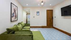 A room with a green sofa, a patterned floor, a wooden door, and a TV mounted on the wall. - Tranquil Stoke-on-trent 4bed, 2 Bath, Parking (Stoke-on-Trent)