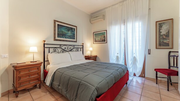 Een slaapkamer met een bed, twee nachtkastjes, een stoel en twee wandgemonteerde airconditioners.