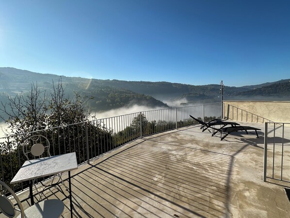 Eine Terrasse mit Blick auf ein Tal und einen Fluss, mit Metallgeländern und einem Tisch mit Stühlen.