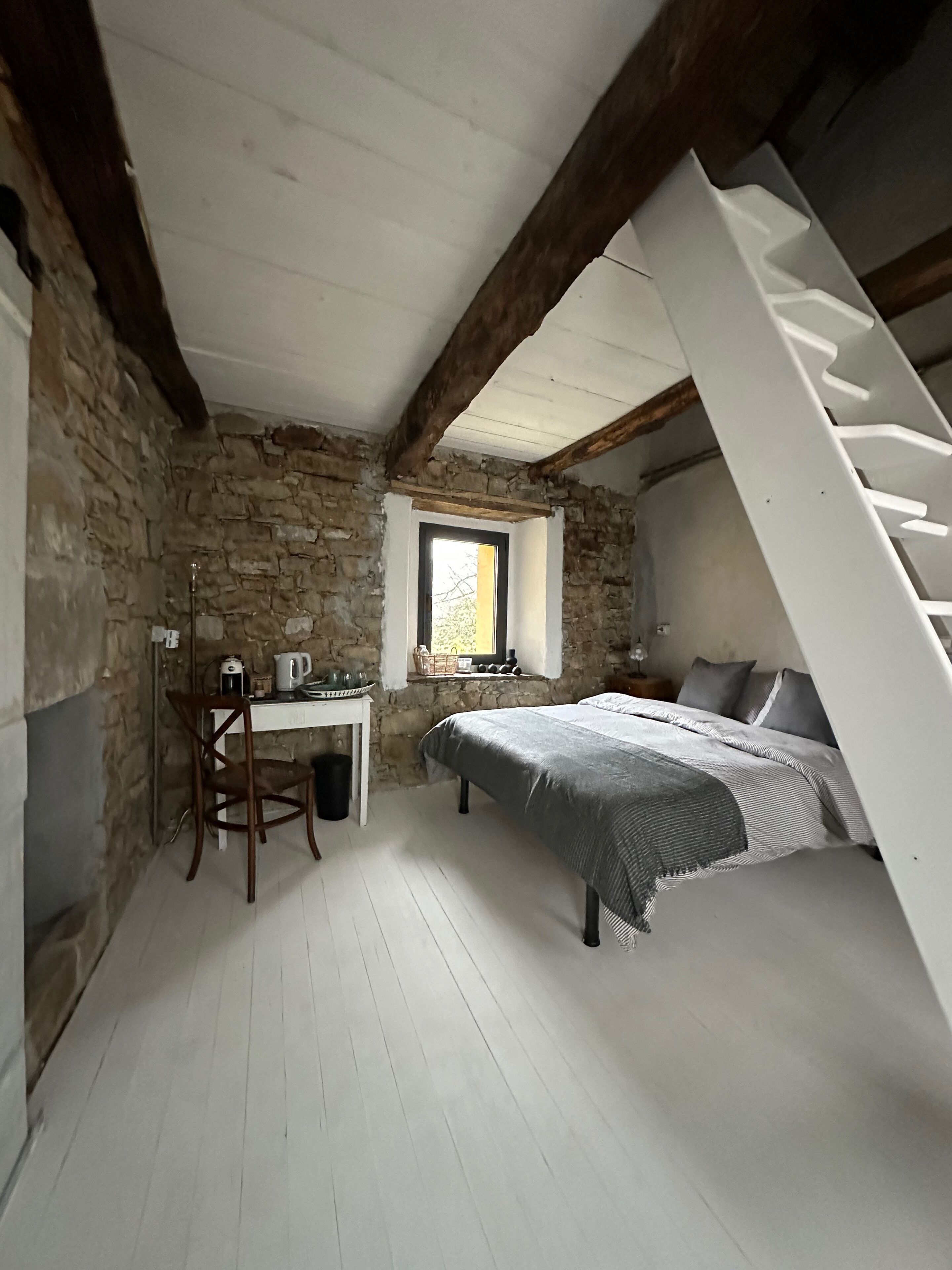 Una habitación con cama, escritorio, silla, ventana y escalera.