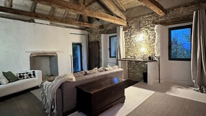 Un'accogliente stanza rustica con travi a vista in legno, un camino in pietra, un divano e un'ampia finestra con tende.