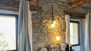 Una stanza rustica con pareti in pietra a vista, travi in legno, uno scaffale con servizio da tè e una finestra con tende.