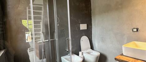 A modern bathroom with a glass shower enclosure, two toilets, a sink, and a black rug.