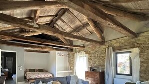 Un interno rustico con travi a vista in legno, un divano grigio, un divano bianco e un muro in pietra.