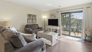 A living room with a sofa, a coffee table, a TV, and a sliding glass door leading to an outdoor area with chairs. - Overlook Paradise Scenic Stay (Branson)