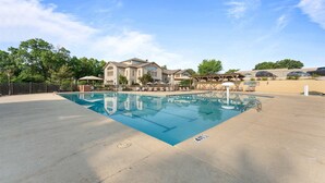 A swimming pool with a clear blue water, surrounded by a concrete deck, and a building with a stone facade in the background. - Overlook Paradise Scenic Stay (Branson)