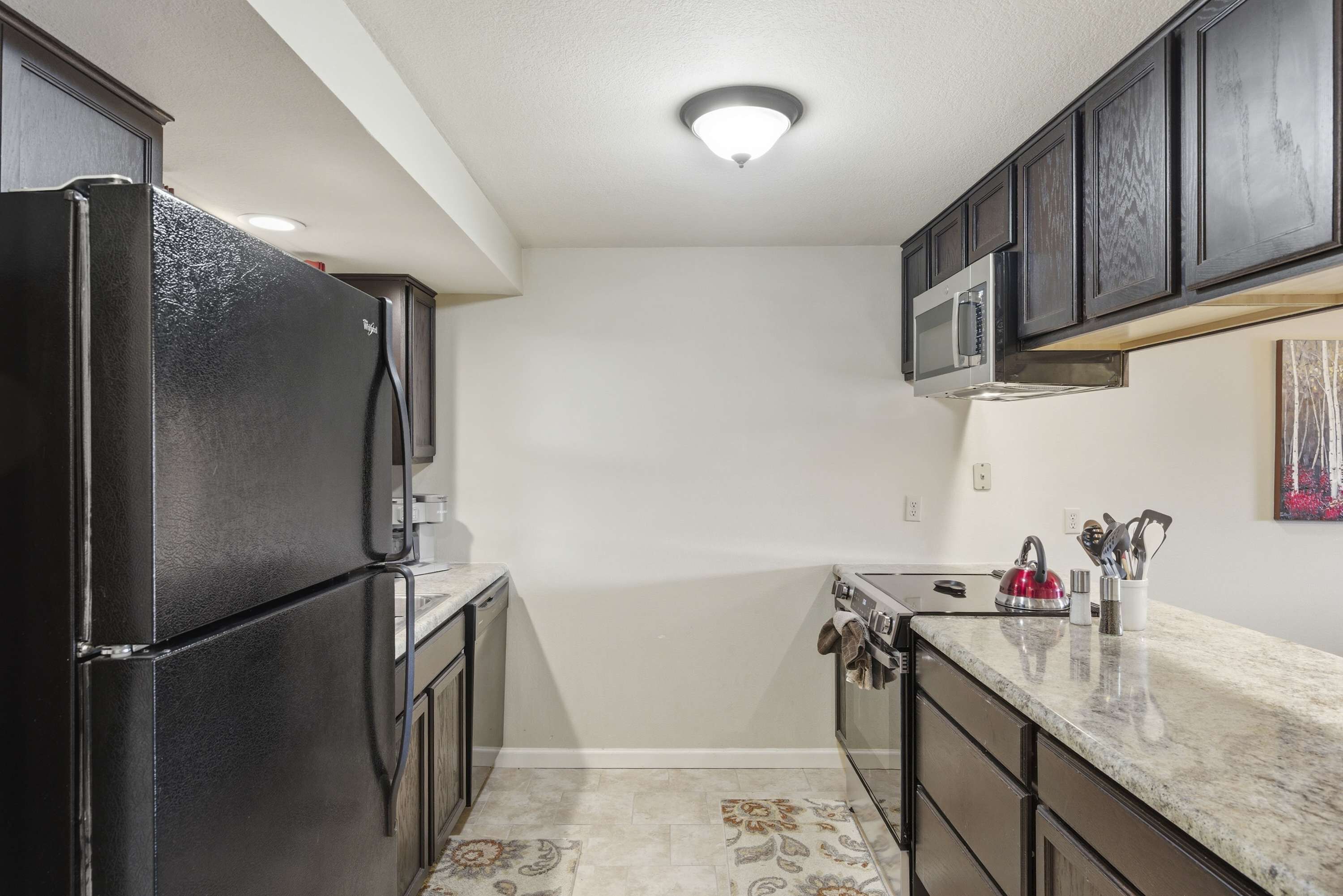 Cocina compacta con armarios oscuros, refrigerador, microondas, lavamanos y encimera con utensilios.
