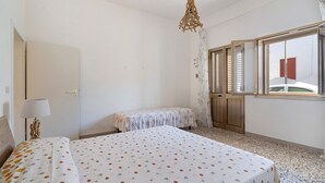 A room with a bed, a small table, a lamp, and a window with shutters.