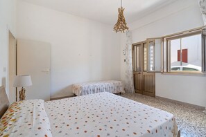 A room with a bed, a small table, a lamp, and a window with shutters.