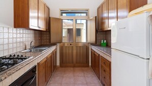 A narrow kitchen with wooden cabinets, a stainless steel sink, a gas stove, and a white refrigerator.