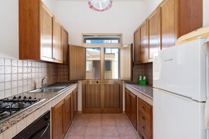 A narrow kitchen with wooden cabinets, a stainless steel sink, a gas stove, and a white refrigerator.