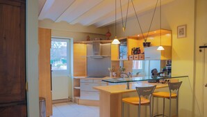 A modern kitchen with a glass island, bar stools, and pendant lighting. - L'Ancien Relais (Genouilly)