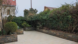 A paved patio area with a brick wall and greenery. - L'Ancien Relais (Genouilly)
