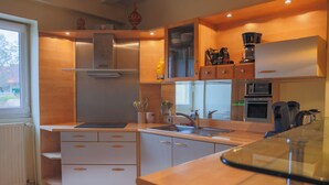 A modern kitchen with wooden cabinets, a stainless steel refrigerator, a built-in oven, and a coffee maker. - L'Ancien Relais (Genouilly)