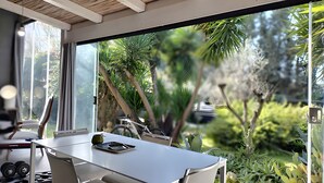 Un espace de repas moderne, avec une table et des chaises, une vue sur le jardin grâce à de grandes fenêtres et un plafond orné de poutres en bois.