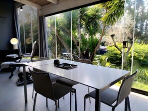 Une chambre moderne avec une grande fenêtre, une table à manger, des chaises, une lampe et un vélo à l’extérieur.