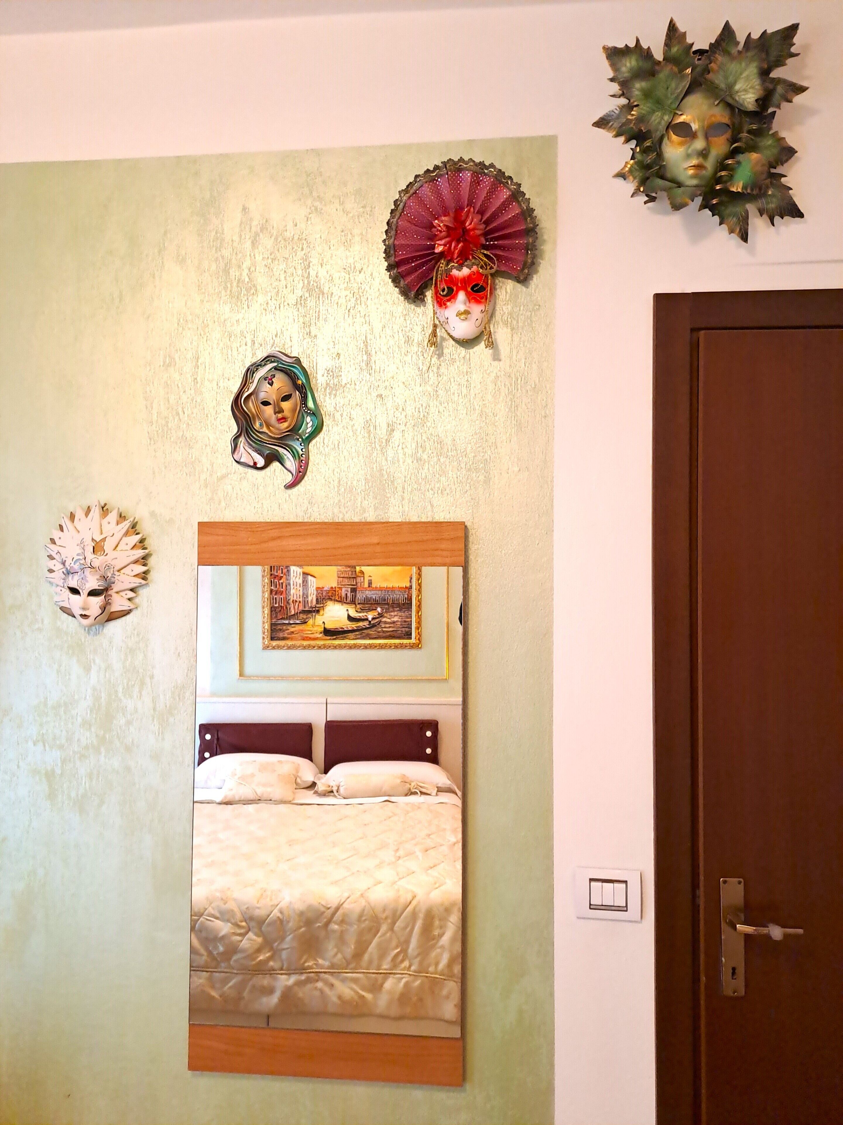 Quarto com cama, um quadro e três máscaras na parede.