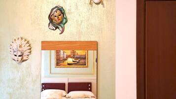 Quarto com cama, um quadro e três máscaras na parede.