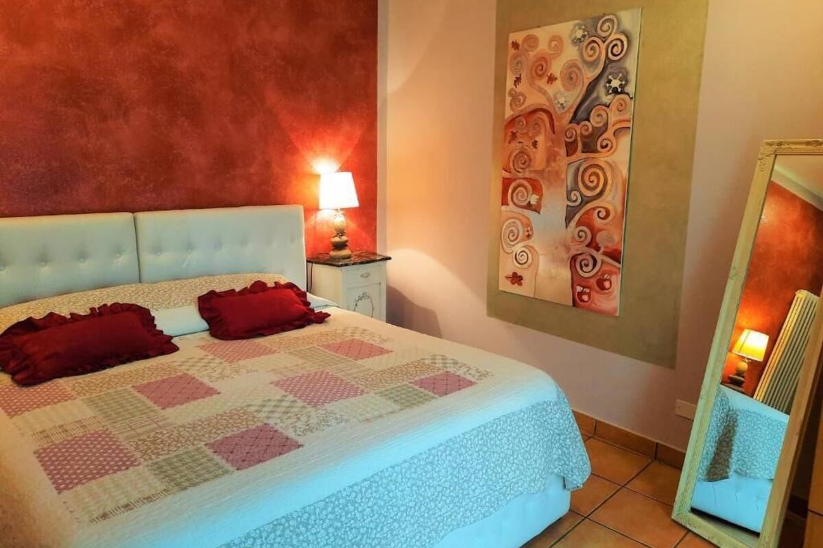 A bedroom with a bed, a nightstand, a wall painting, and a mirror.