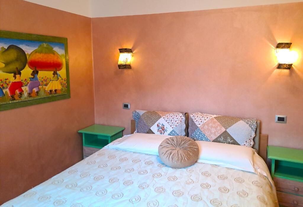 A bedroom with a bed, two nightstands, a painting on the wall, and two wall-mounted lights.