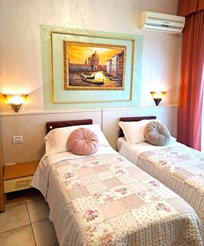 Ein Hotelzimmer mit zwei Betten, einem Stadtbildgemälde, Wandleuchten und einer Klimaanlage.