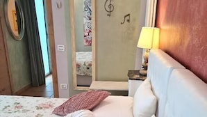 A bedroom with a bed, pillows, a nightstand, a lamp, a mirror, and a wall with musical notes. - Boutique Hotel Florivana (San Pietro in Cariano)