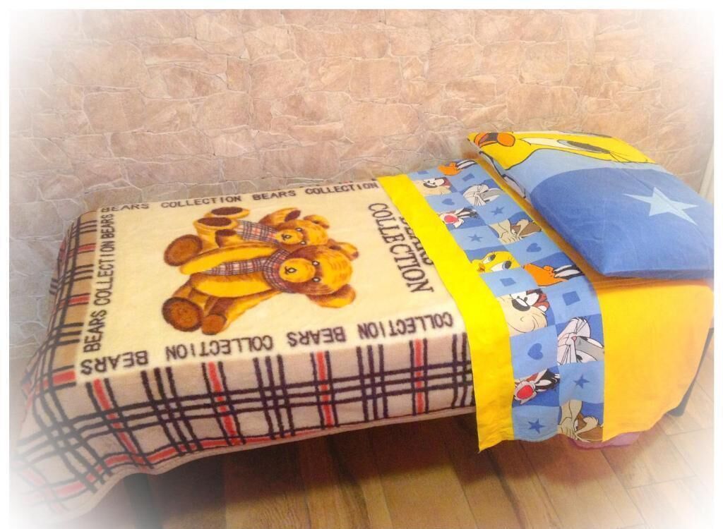 A bed with a plaid-patterned blanket and a yellow pillow with cartoon characters.