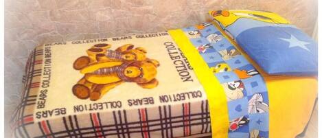A bed with a plaid-patterned blanket and a yellow pillow with cartoon characters.