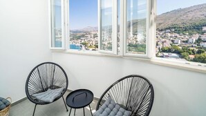 Ein Balkon mit drei schwarzen Stuhlgestellen und einem kleinen Tisch, mit Blick auf eine Stadt und Hügel.