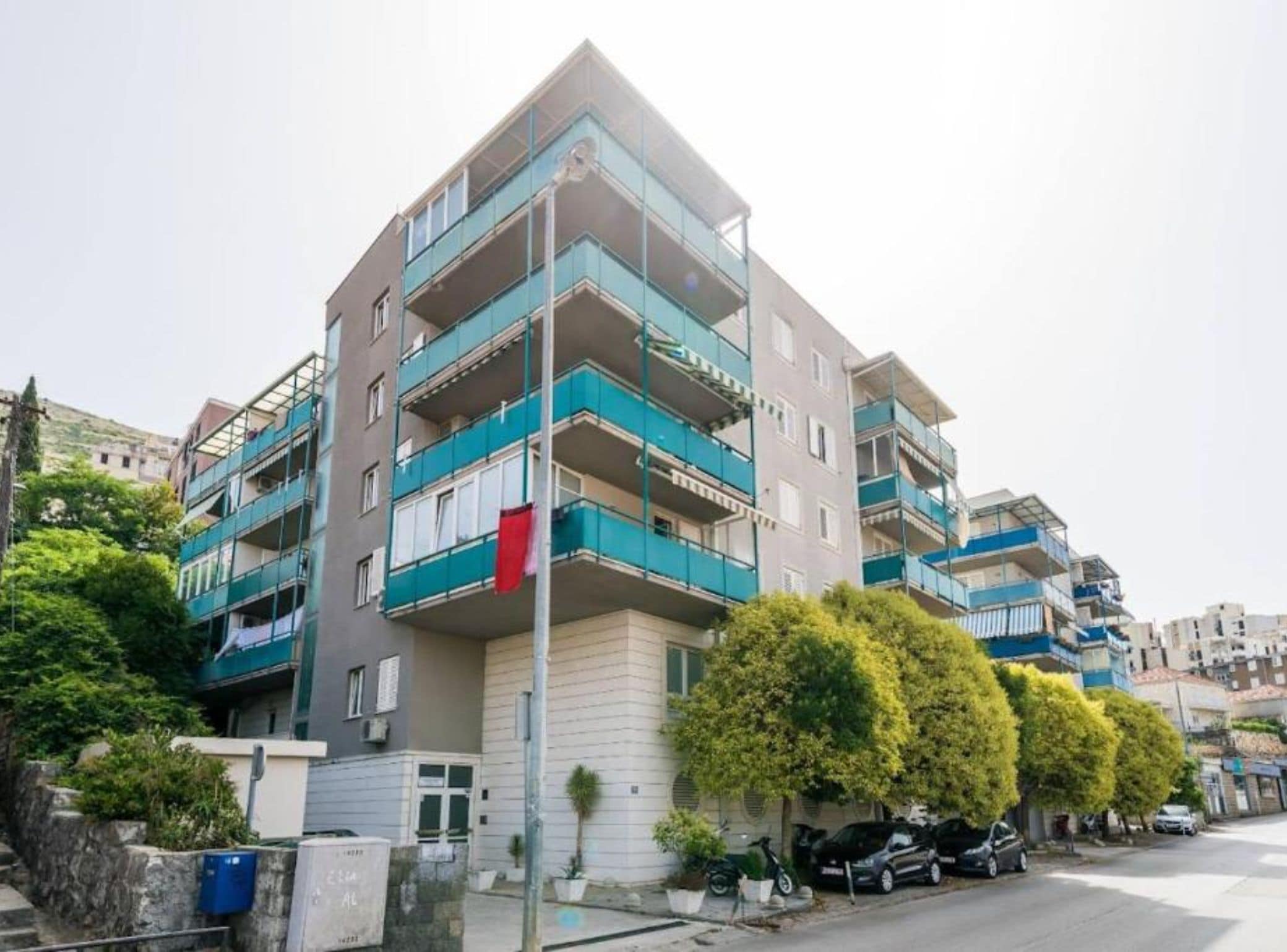 A multi-story residential building with balconies, a street view, and parked cars.