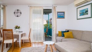 Ein Wohnzimmer mit einer Couch, einem Esstisch mit Stühlen, einer Uhr und einem Bild an der Wand.