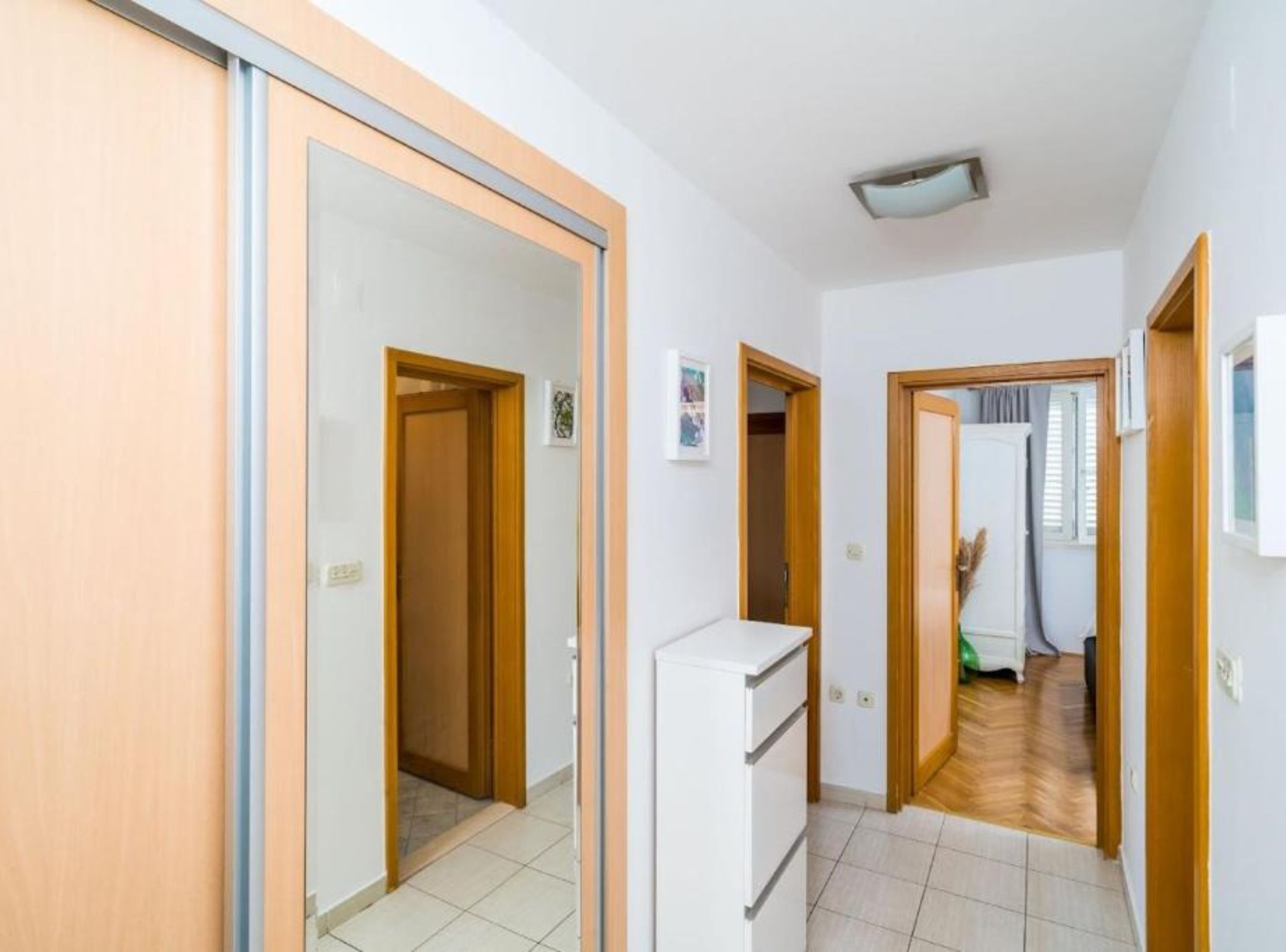 Un couloir avec des portes en bois, un réfrigérateur blanc et un sol carrelé.