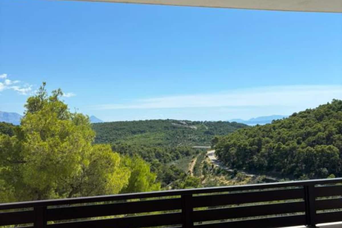 A balcony with a view of a forested hillside and a road.